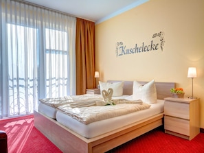 Ein Hotelzimmer mit einem Bett, zwei Nachttischen, einer Wandleuchte, einer Obstschale und einem großen Fenster mit Vorhängen.