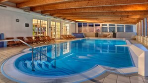 Une piscine intérieure avec des poutres en bois, des chaises longues et une terrasse ensoleillée.