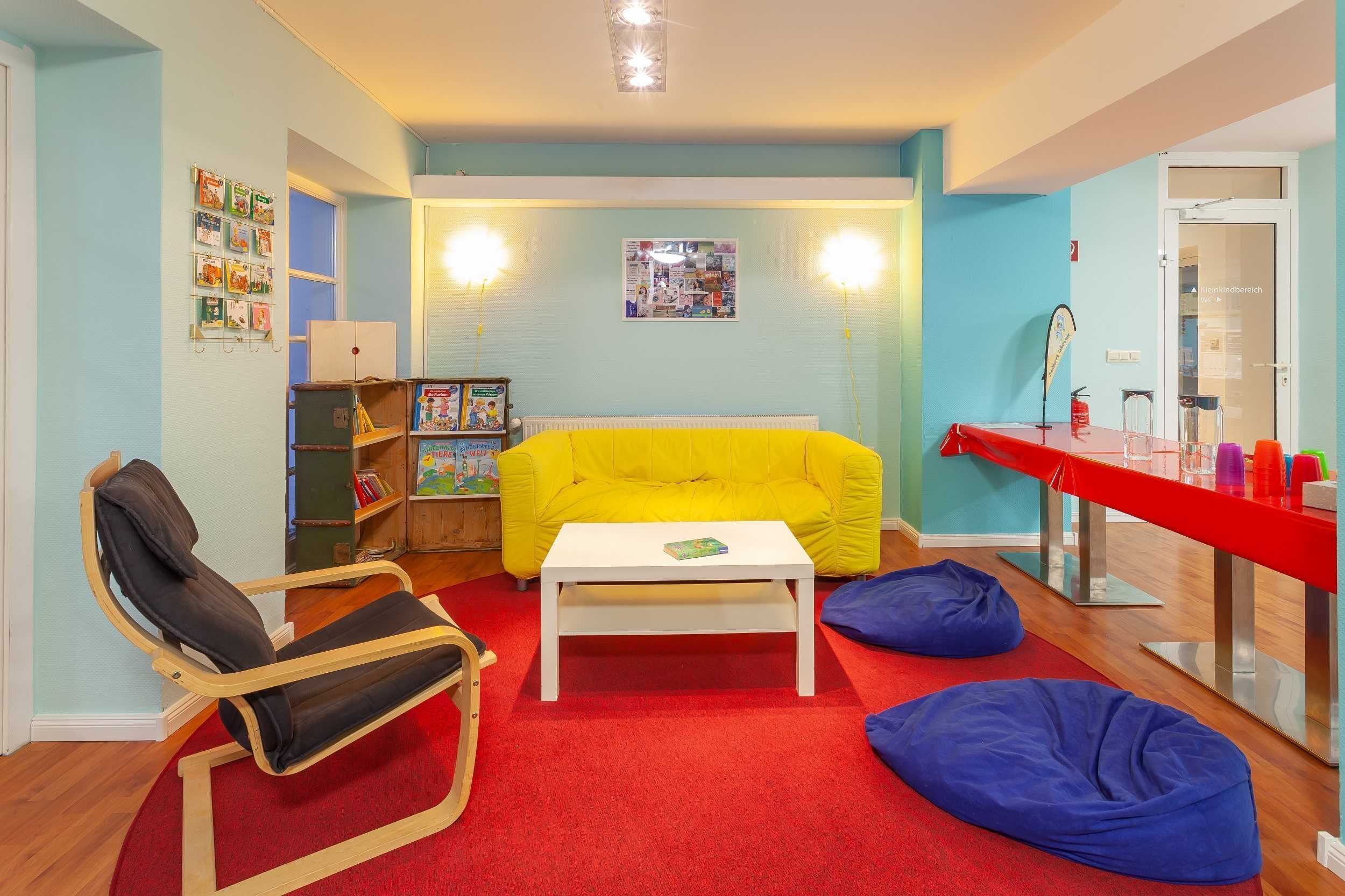 Ein Zimmer mit einem gelben Sofa, einem weißen Couchtisch, einem roten Teppich, einem Holzstuhl und einem Bücherregal.