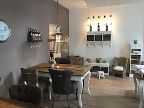 A dining area with a wooden table, chairs, a hanging light fixture, wine bottles, and a clock on the wall. - Category II (Hotel) - Suite Hotel Binz Rugen Familotel (Binz)
