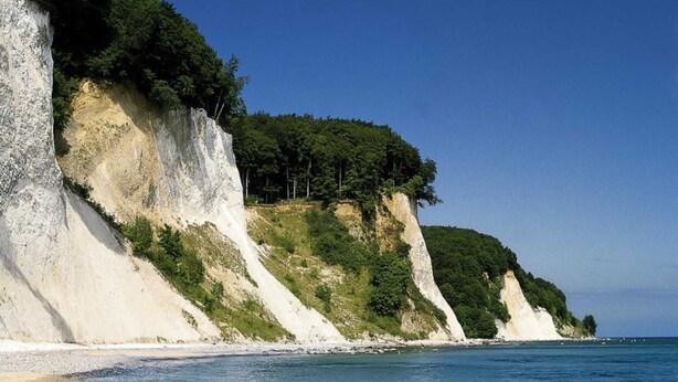Une plage côtière bordée de falaises blanches et baignée par une mer d’un bleu limpide.