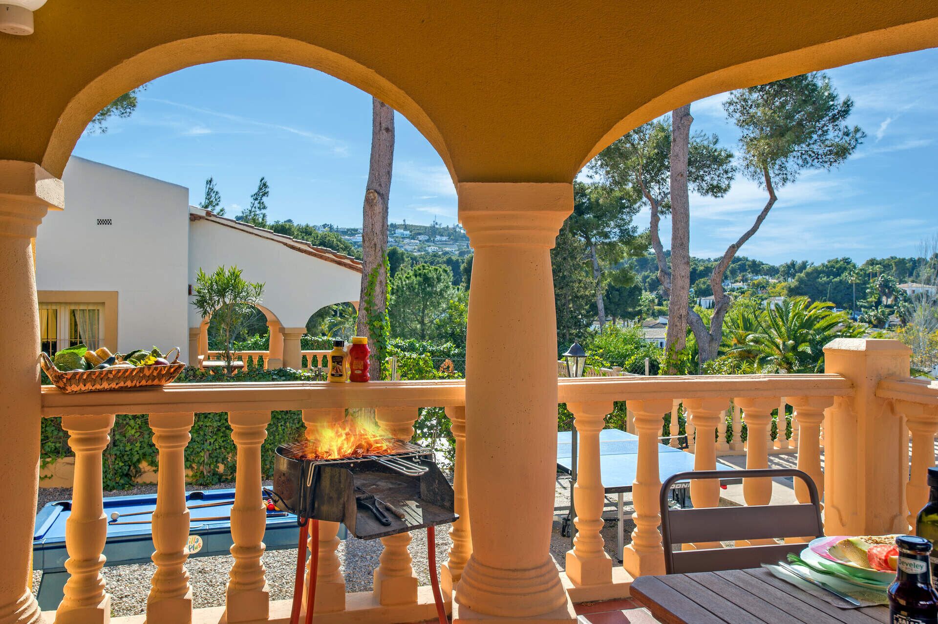 A patio with a grill, outdoor seating, and a view of a white building and trees.