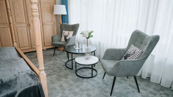 Una habitación con cama, armario de madera, dos sillones, una mesita redonda con un florero y una lámpara.