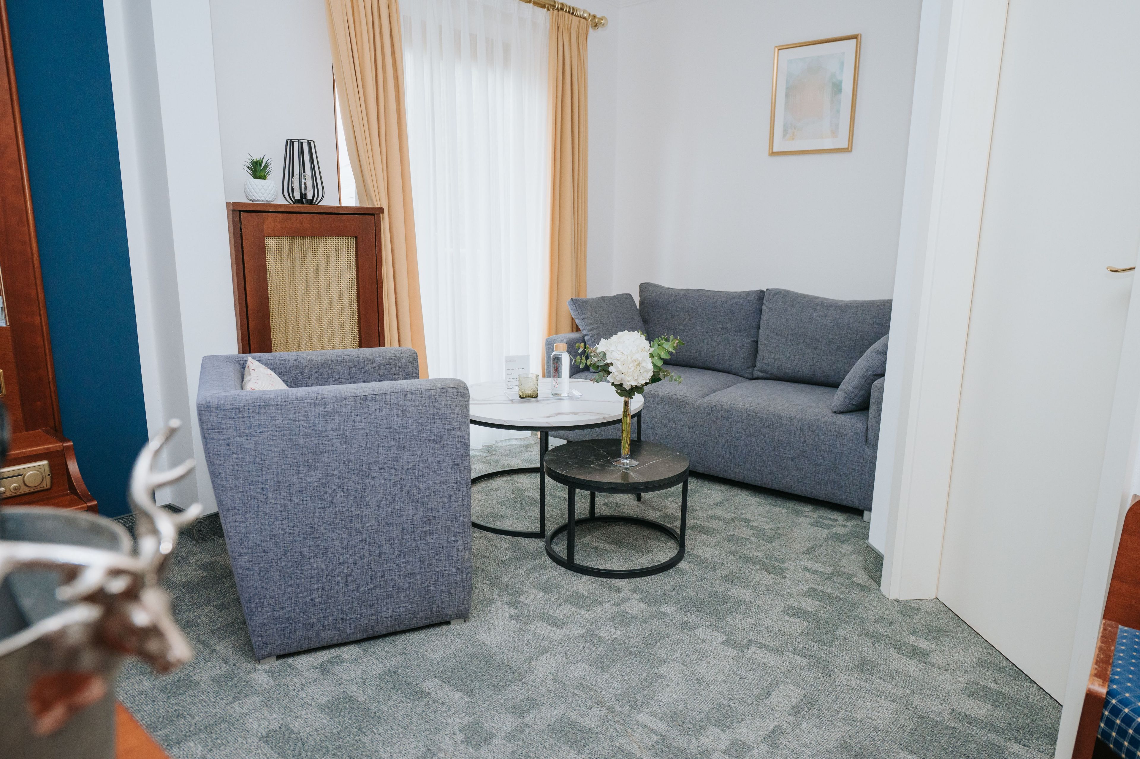 Un salon moderne avec un canapé gris, une table basse ronde et une petite table d’appoint sur laquelle est posé un vase de fleurs.