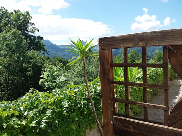 A wooden structure with a grid pattern, surrounded by lush greenery and a mountainous backdrop.