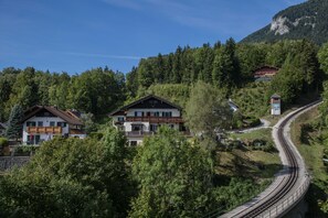 Een hotel aan de berghelling met meerdere gebouwen, omringd door dicht bos en een spoorlijn.