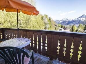 Una terraza de madera con una mesa y sillas, una valla decorativa y vistas a la montaña.