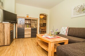 Ein Wohnzimmer mit Holztisch, einer Couch und einem Fernseher auf einem Schrank.