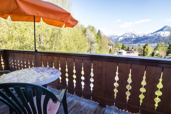 Een houten terras met een tafel en stoelen, een houten omheining met decoratieve details, en een uitzicht op de bergen in de achtergrond.