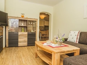 A living room with a wooden coffee table, a sofa, and a kitchen area with cabinets and a television.