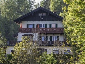 Een chalet met twee verdiepingen en een balkon, omgeven door bomen.