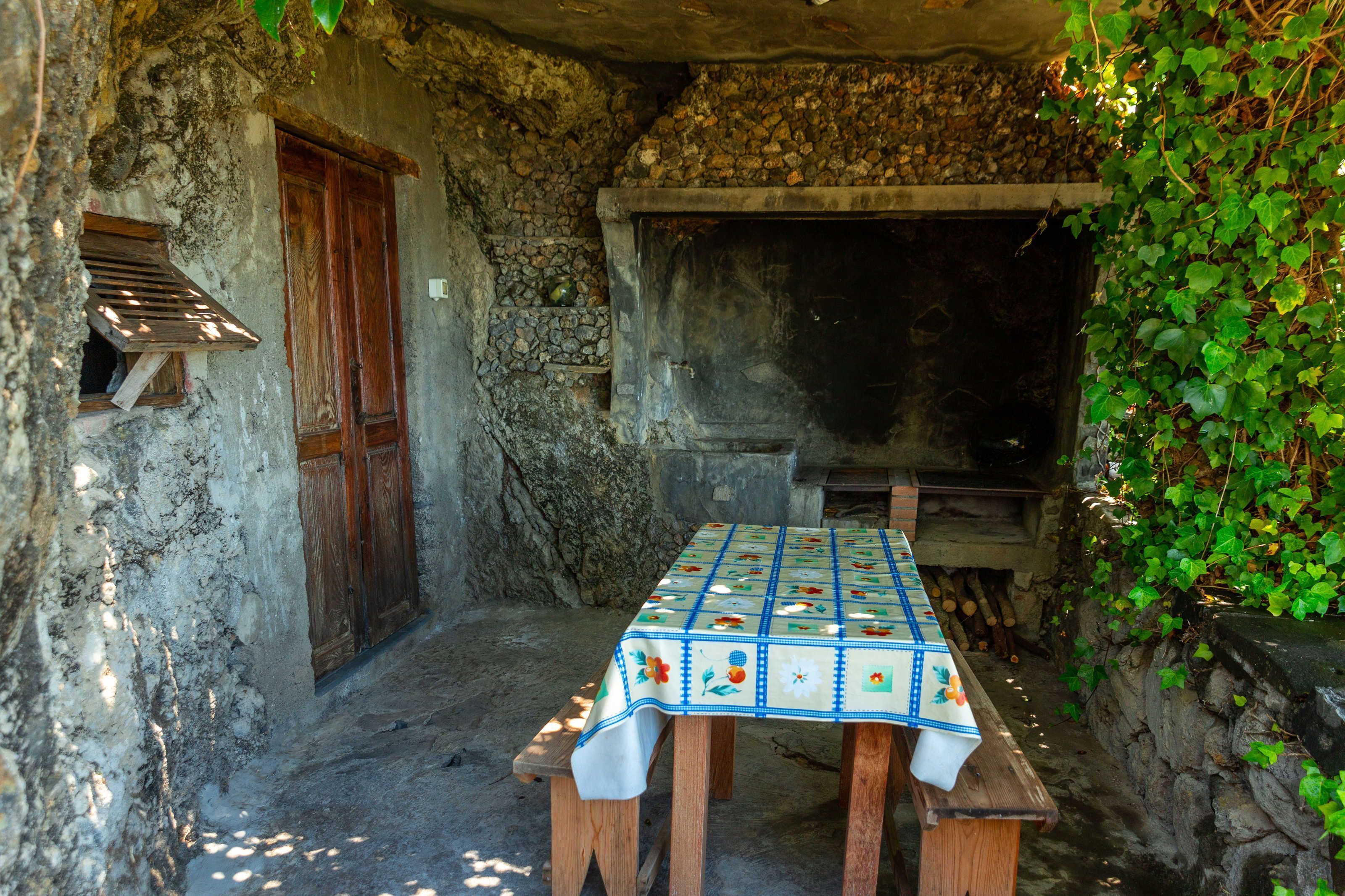 A rustic outdoor dining area with a stone wall, wooden door, and a table with a floral tablecloth.