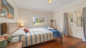 Ein Schlafzimmer mit einem hölzernen Bett, einem Fenster mit Ausblick, einer Tür mit Vorhängen und einem Gemälde an der Wand.