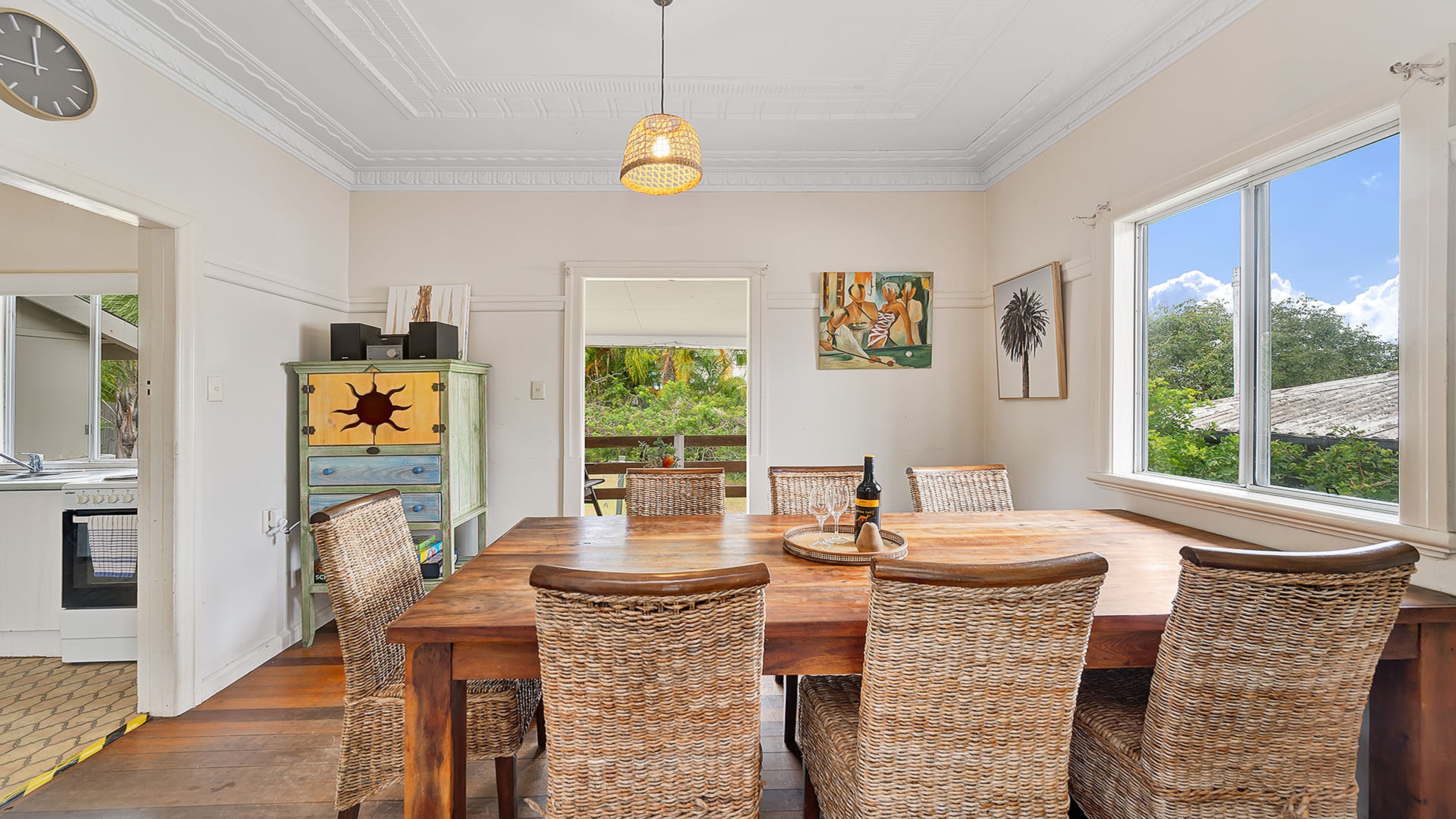 A dining area with a wooden table and wicker chairs, a hanging light fixture, and artwork on the walls.