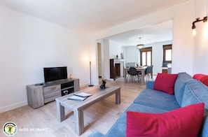 Ein modernes Wohnzimmer mit einem Flachbildfernseher, einem Holztisch und einem grauen Sofa mit roten Kissen.