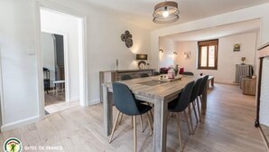 Un coin repas avec une table et des chaises en bois, un luminaire suspendu et une cuisine en arrière-plan.