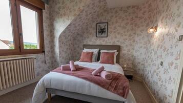 A bedroom with a bed, a nightstand, a window, and a wall-mounted light fixture.