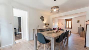 A dining area with a wooden table and chairs, a pendant light, and a kitchen in the background.