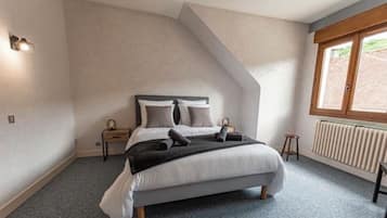 A bedroom with a bed, a nightstand, a window, and a radiator.