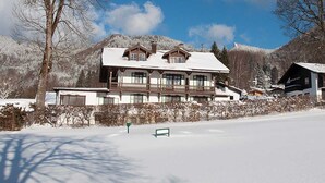 A large, traditional chalet-style building with a snow-covered roof, surrounded by a snowy landscape and mountains. - Double Room South - Gästehaus Florian (Tegernsee)
