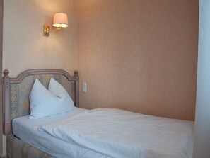 A single bed with a headboard, a wall-mounted light, and a plain wall.
