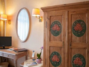 A room with a wooden wardrobe, a desk with a computer, a mirror, and wall-mounted lamps.