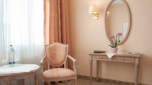 Une chambre d’hôtel avec une table ronde, une chaise, un bureau avec une lampe, un miroir et une plante en pot.