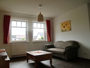 A room with two windows, a sofa, a wooden table, and a hanging light fixture.