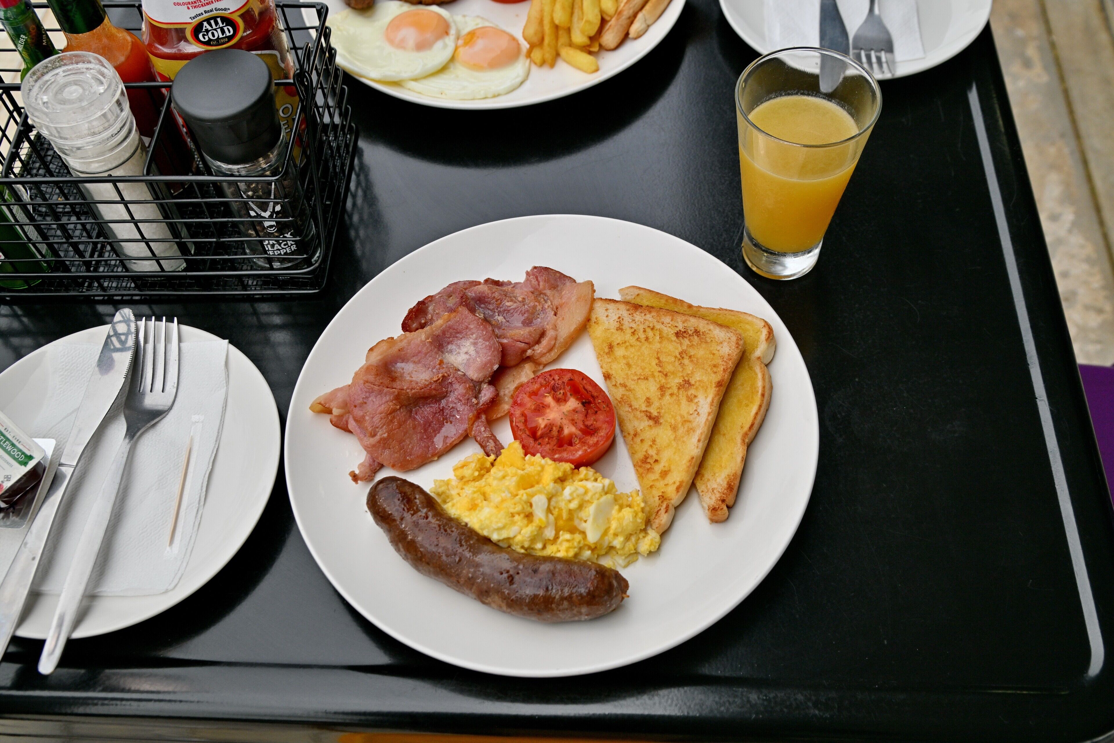 A breakfast tray with eggs, bacon, sausage, toast, and a glass of orange juice.