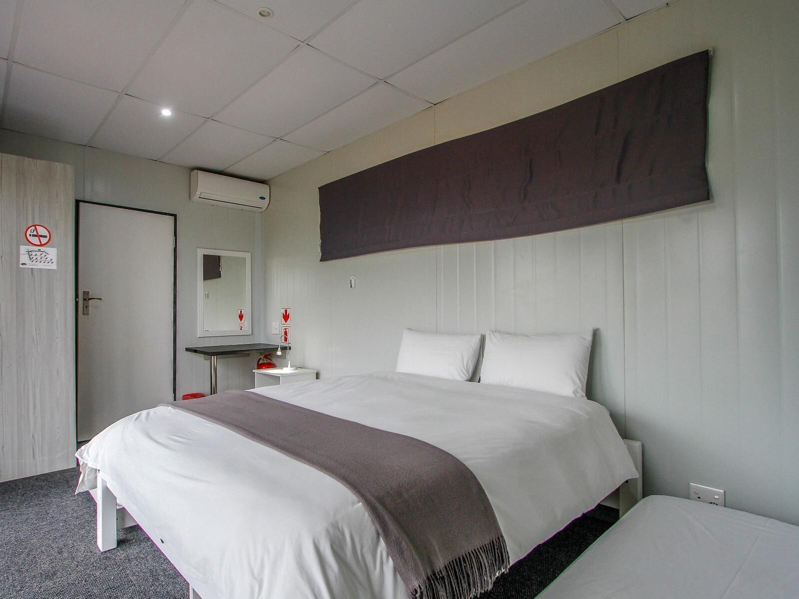 A hotel room with a large bed, a bedside table, a mirror, and a wall-mounted air conditioner.