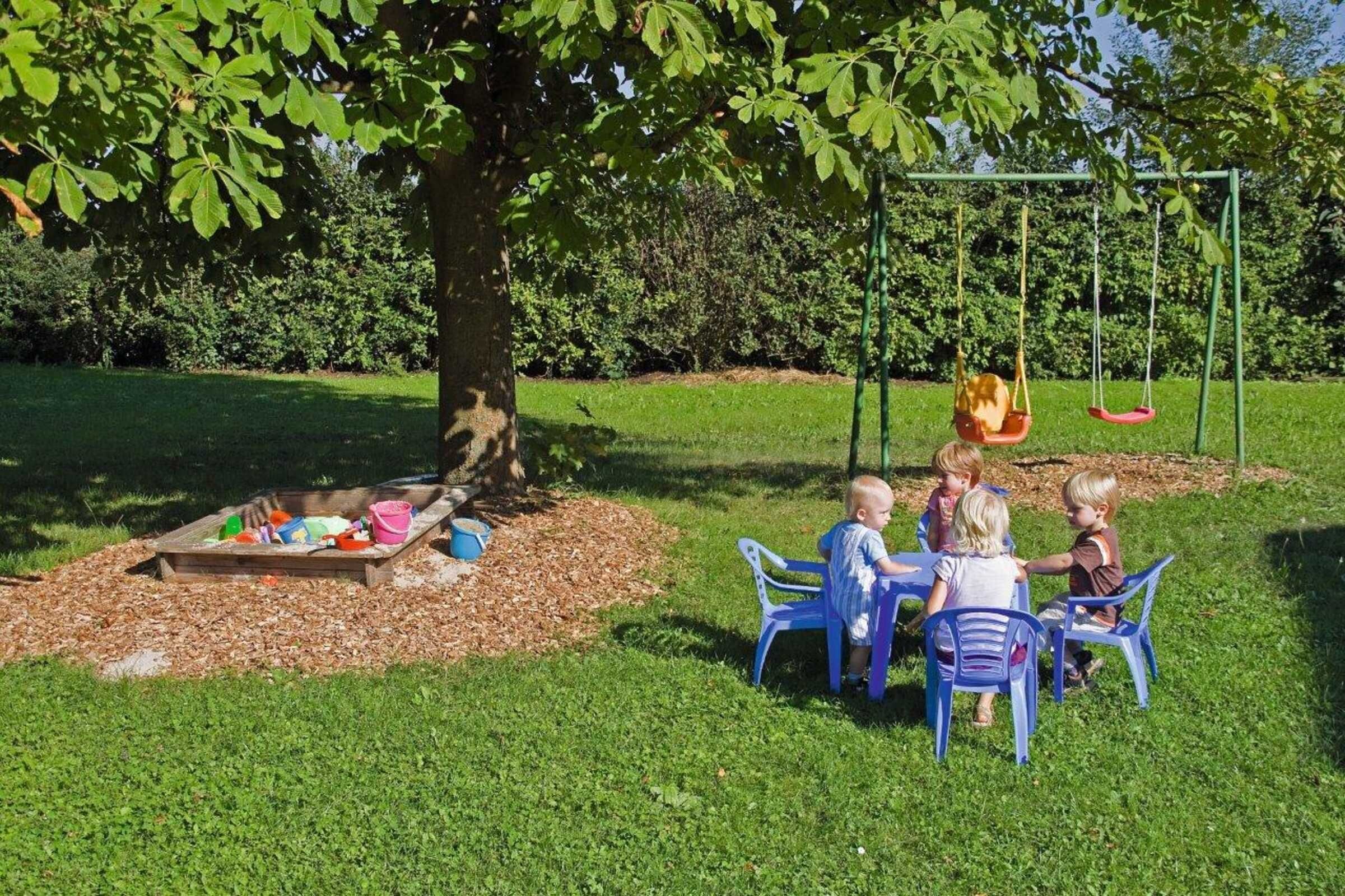 A group of children playing under a tree with a swing set in a park.