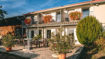 Ein zweistöckiges Gebäude mit Balkon, Sitzgelegenheit im Freien und Kübelpflanzen.