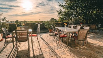 Eine Terrasse im Freien mit Tisch und Stühlen, umgeben von viel Grün und blauem Himmel.