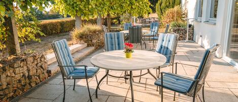An outdoor patio with a round table and chairs, surrounded by stone walls and greenery.