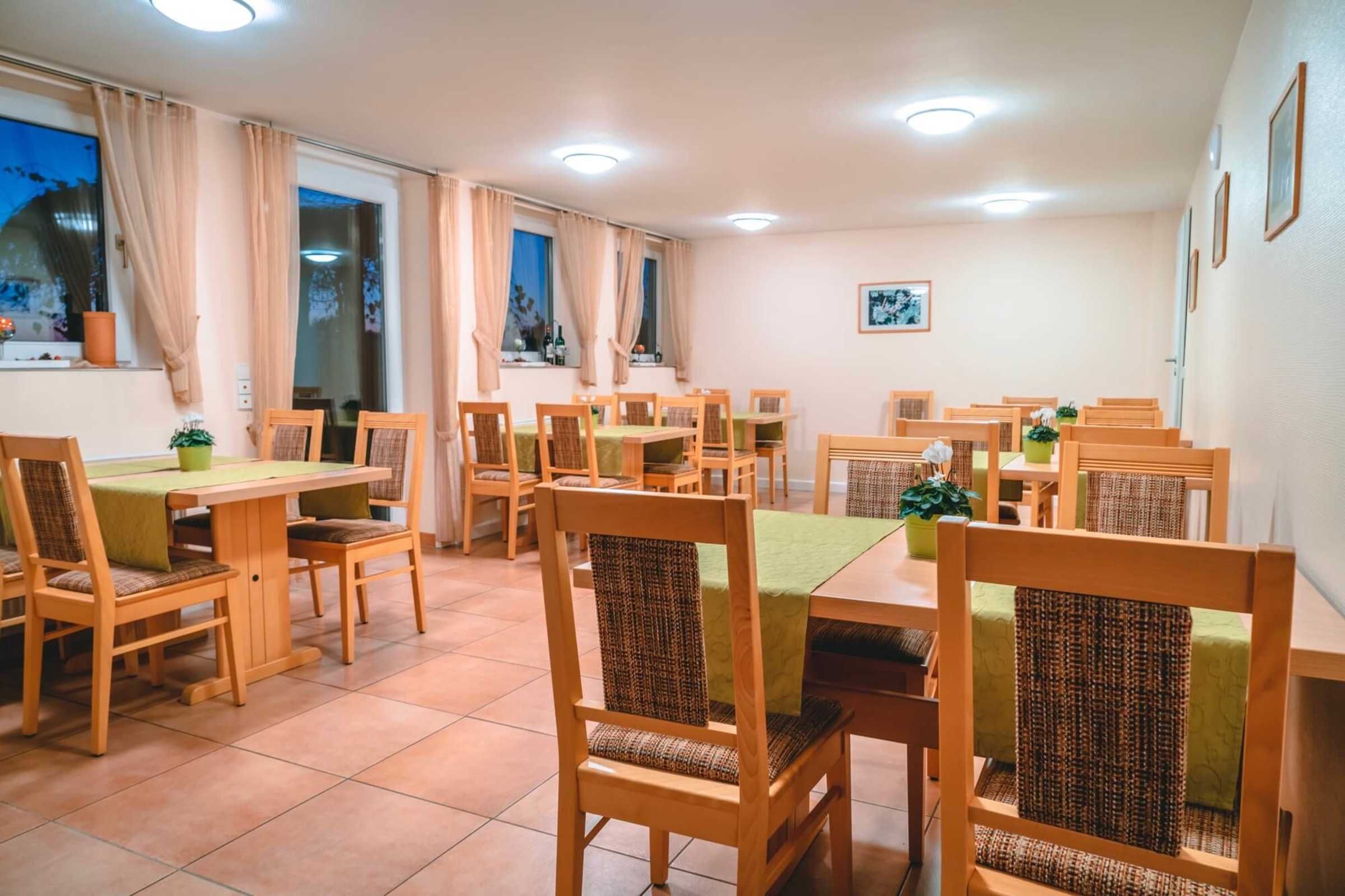 Ein Essbereich mit mehreren Holztischen und Stühlen, einer grünen Tischdecke und einem Blumentopf auf jedem Tisch.