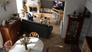 Una sala de estar con chimenea, sofá, televisor y comedor con mesa y sillas.