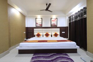 Un dormitorio con cama, ventilador de techo, cabecera con almohadones decorativos y cuadros en la pared.