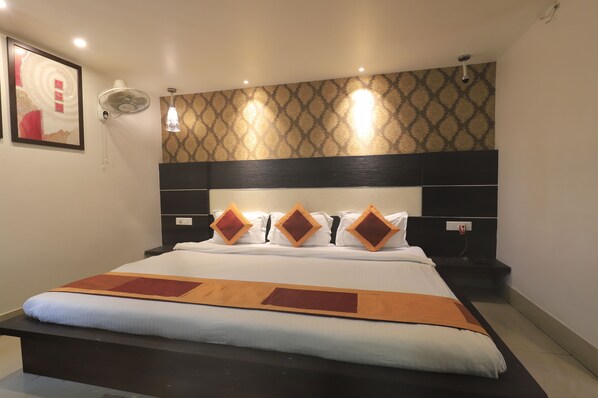Habitación de hotel con una cama grande, un ventilador de pared y un papel tapiz estampado.
