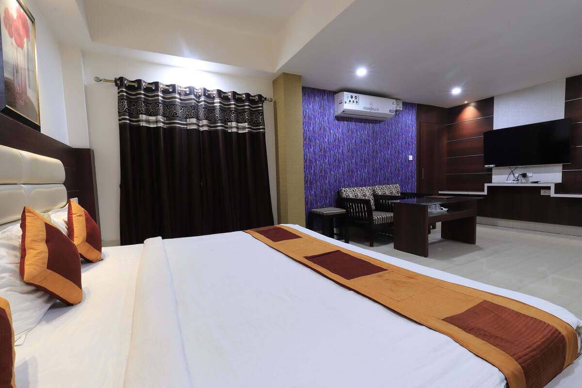 A hotel room with a large bed, a desk, a chair, a flat-screen TV, and an air conditioning unit.
