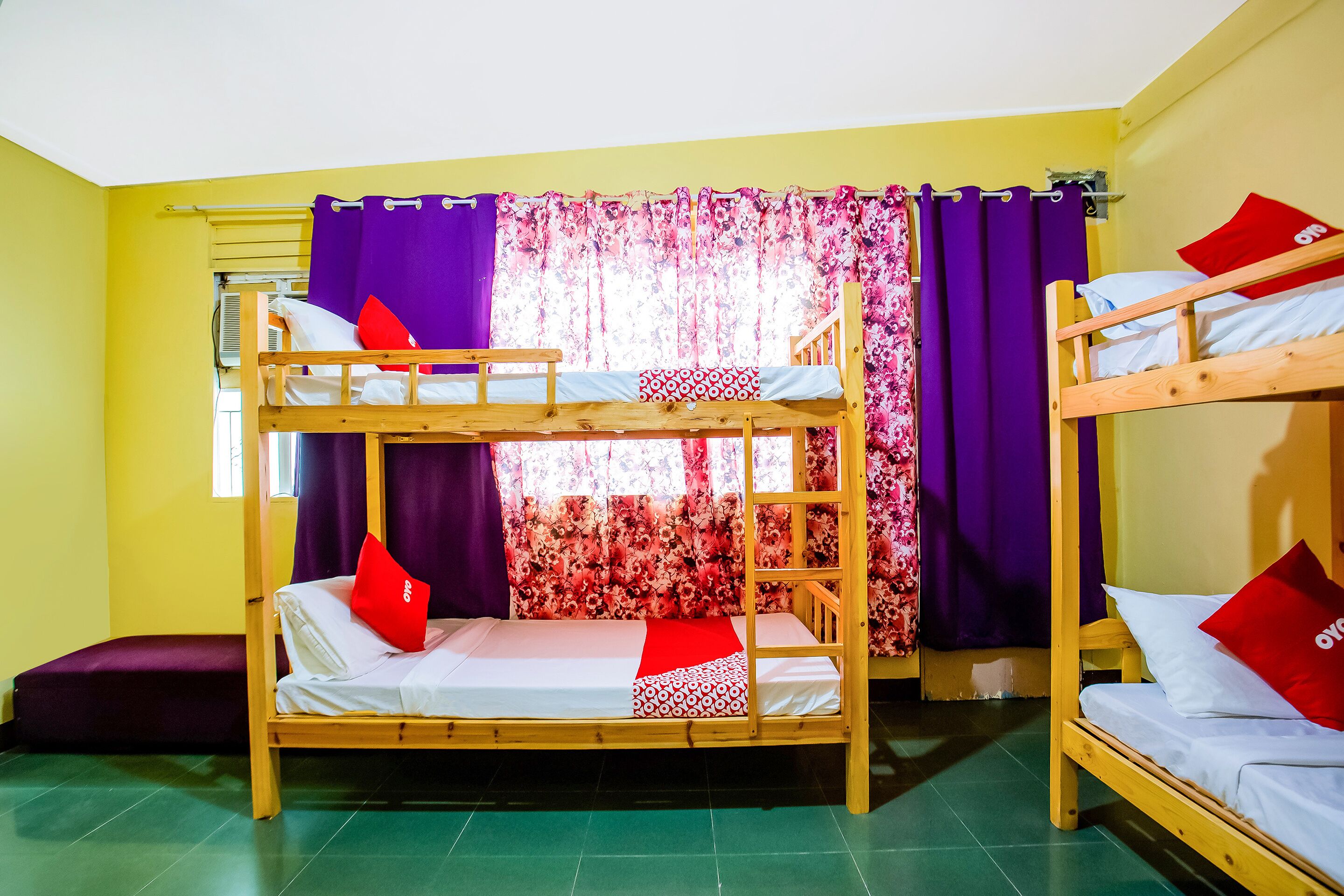 A dormitory room with two bunk beds, a purple curtain, and a floral window treatment.