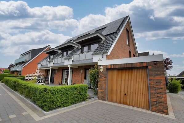 Una moderna casa a due piani con tetto spiovente, porta garage in legno e un curato giardino antistante con siepi.
