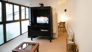 Ein Wohnzimmer mit einem großen Fernseher auf einer schwarzen Unterhaltungsecke, einem kleinen Holztisch und einem Sessel.