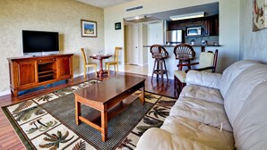 A living room with a TV, wooden entertainment unit, and a dining area with chairs and a table. - Regatta Beach Club C713 '90 day min stay with 2 week lead time' (Clearwater Beach)