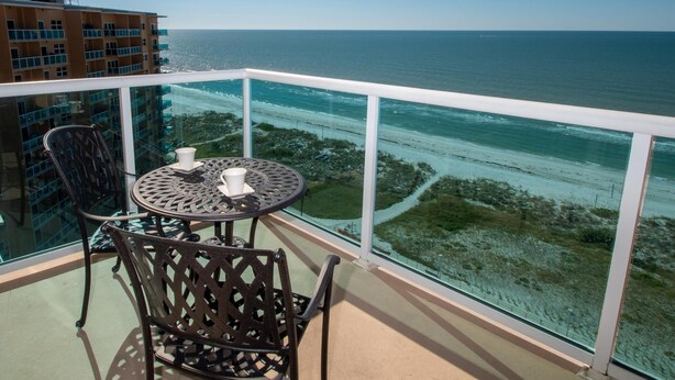 A balcony with a table and chairs, overlooking a beach and ocean. - Regatta Beach Club C1009 '90 day min stay with 2 week lead time' (Clearwater Beach)