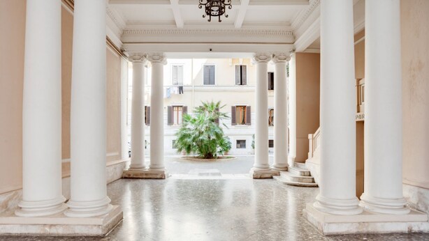 A corridor with white columns, a central potted plant, and a view of buildings in the background. - GuestHost - Elegant and roomy apartment equipped with every comfort to accommodate up to 6 people, with 3 bedrooms and 2 bathrooms. The location is enviable: in front of the lively promenade of Bari, the beating heart of the city with its events, a 2-min (Bari)