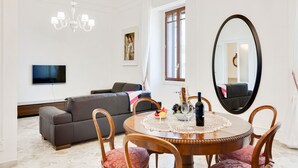 A living room with a sofa, a dining table with chairs, a TV mounted on the wall, a chandelier, and a large mirror. - GuestHost - Elegant and roomy apartment equipped with every comfort to accommodate up to 6 people, with 3 bedrooms and 2 bathrooms. The location is enviable: in front of the lively promenade of Bari, the beating heart of the city with its events, a 2-min (Bari)