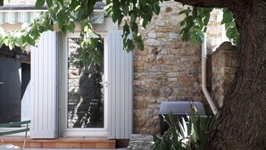 A stone building with a wooden door and a window, surrounded by greenery and a tree. - Charmante maisonnette rénovée proche Uzès Charming little house near Uzès (Foissac)
