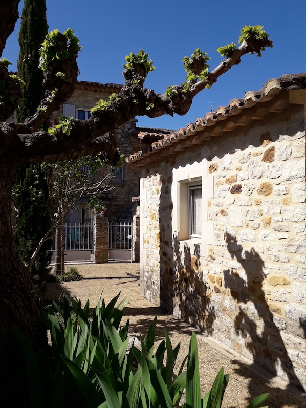 Un bâtiment en pierre avec un toit en tuiles, une fenêtre et un arbre aux feuilles vertes au premier plan.