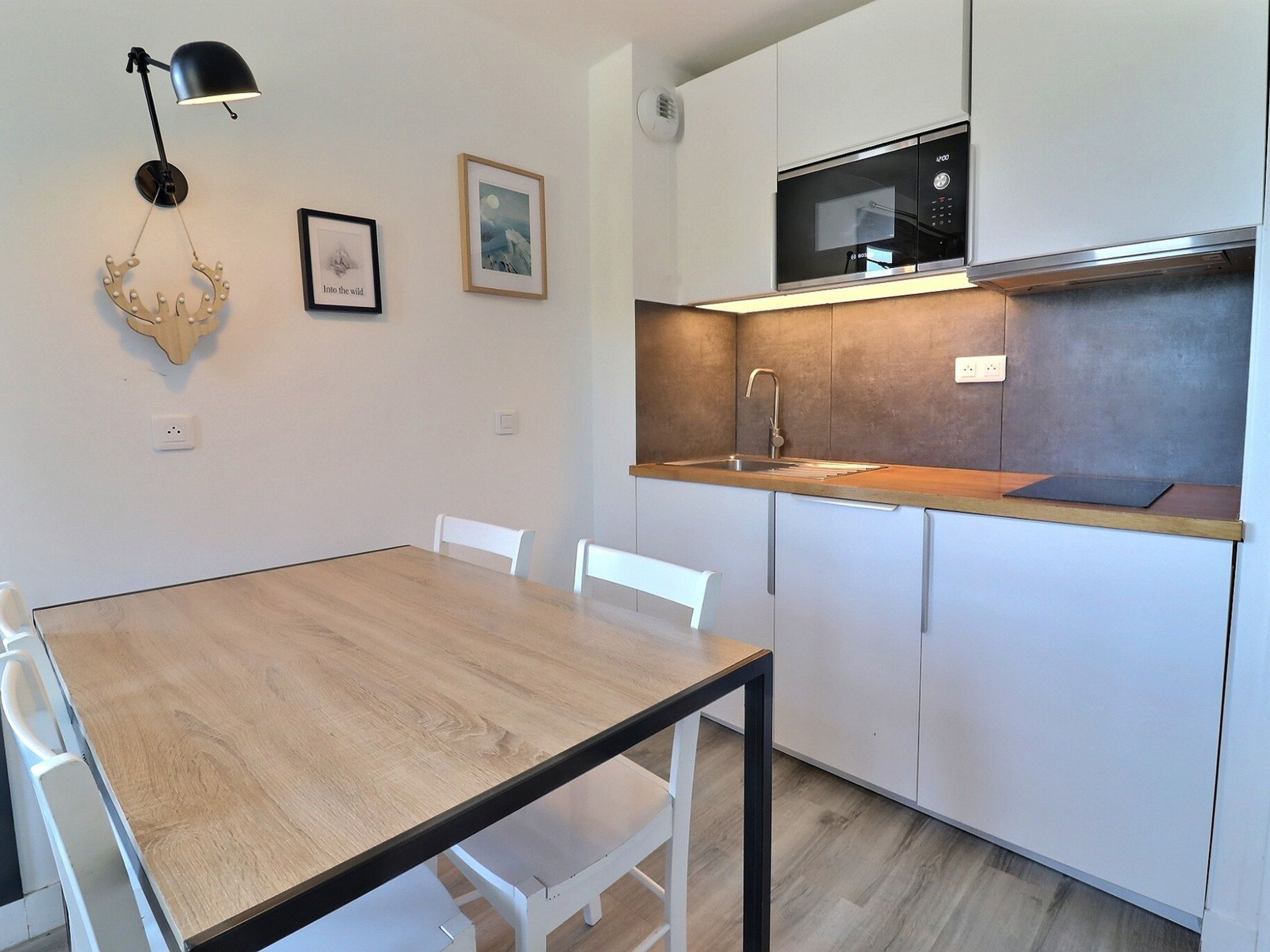 A modern kitchen with a wooden table and white chairs, a microwave, and a sink.