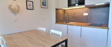 Eine moderne Küche mit einem Holztisch, weißen Stühlen, einer Mikrowelle und einem Spülbecken.